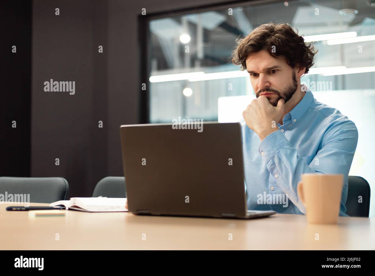 Focused man using laptop sitting at desk in office Stock Photo