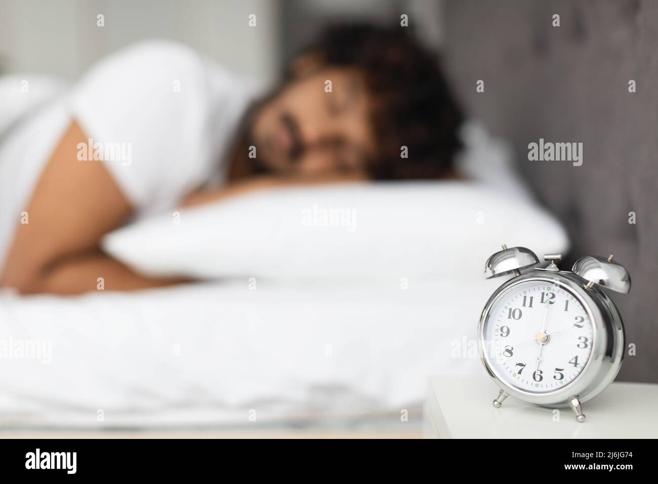 Selective focus on alarm on bedside over sleeping man Stock Photo