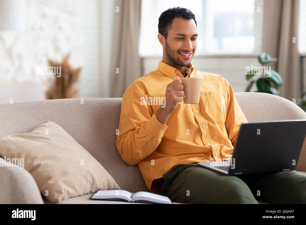 Smiling Arab man watching video on computer, drinking coffee Stock Photo