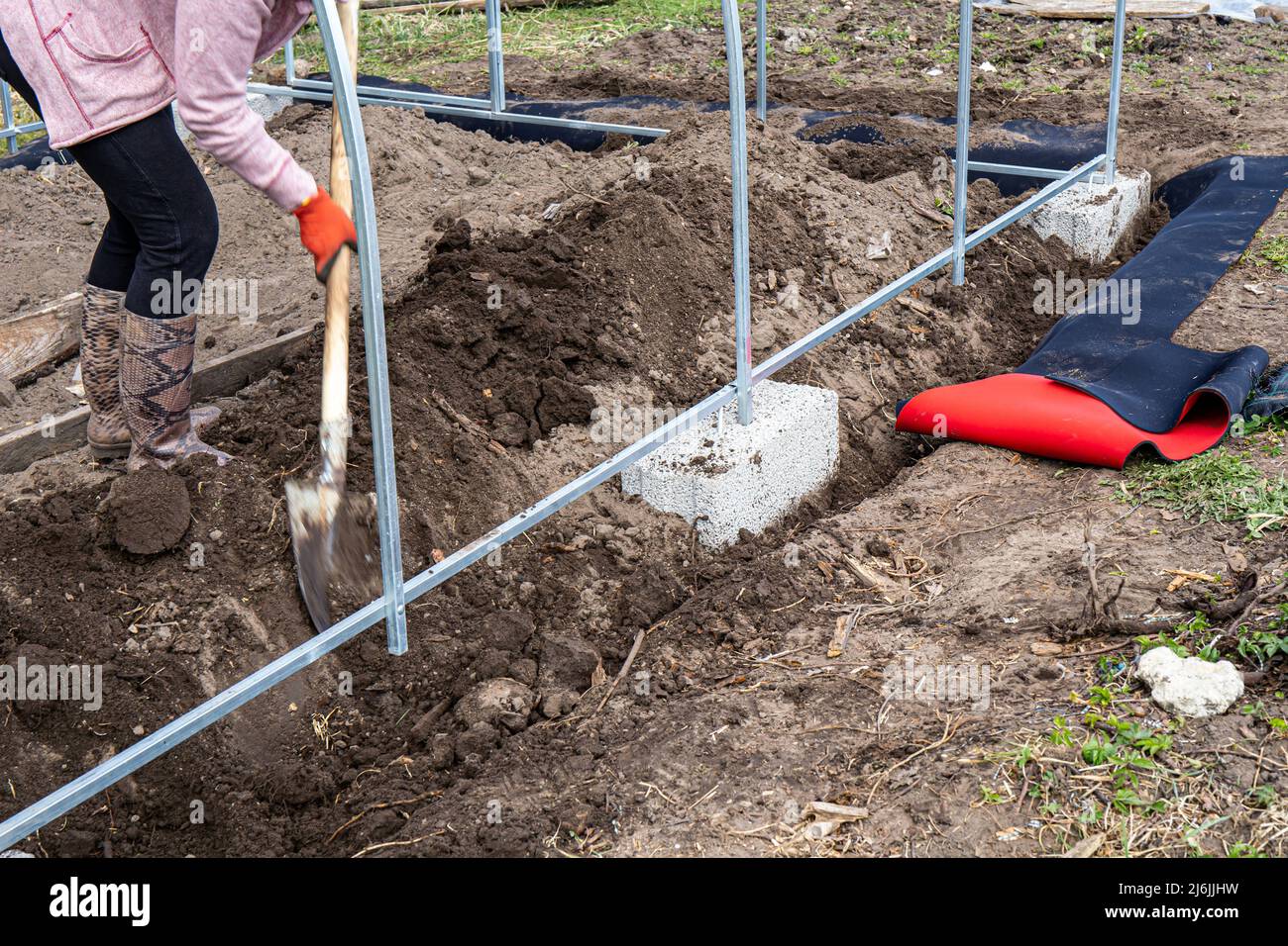 Woman gardener building  base of the greenhouse outdoors in spring. Stock Photo