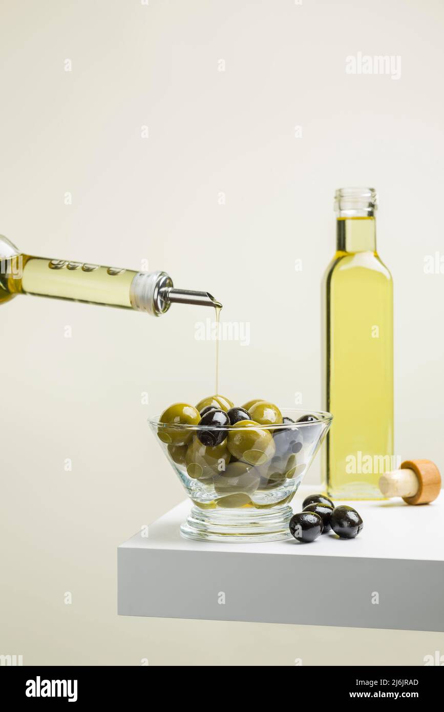 Big green and black olives in glass bowl on shelf with oil bottle Stock Photo