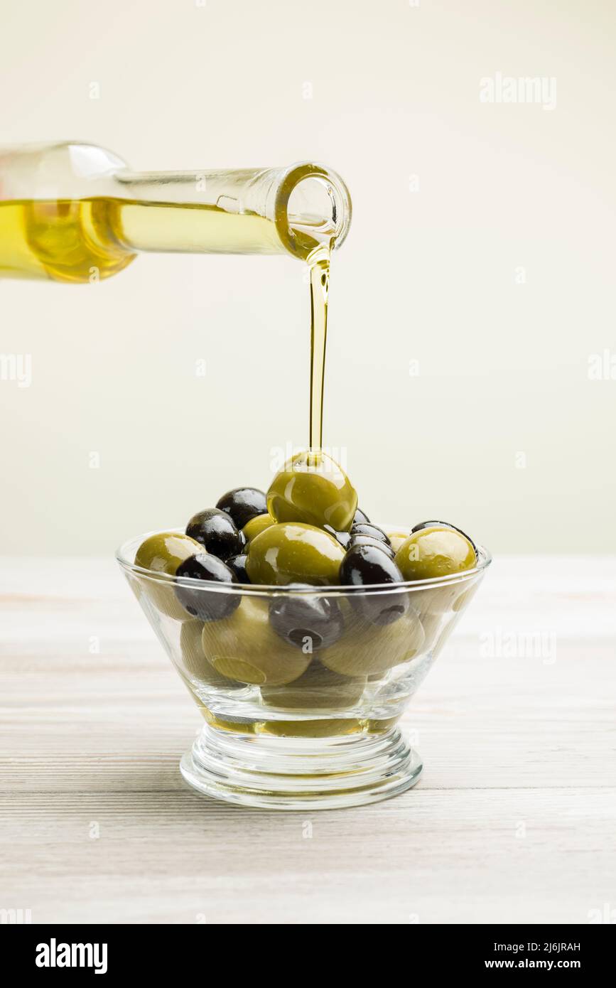 Big green and black olives in glass bowl on wooden table Stock Photo