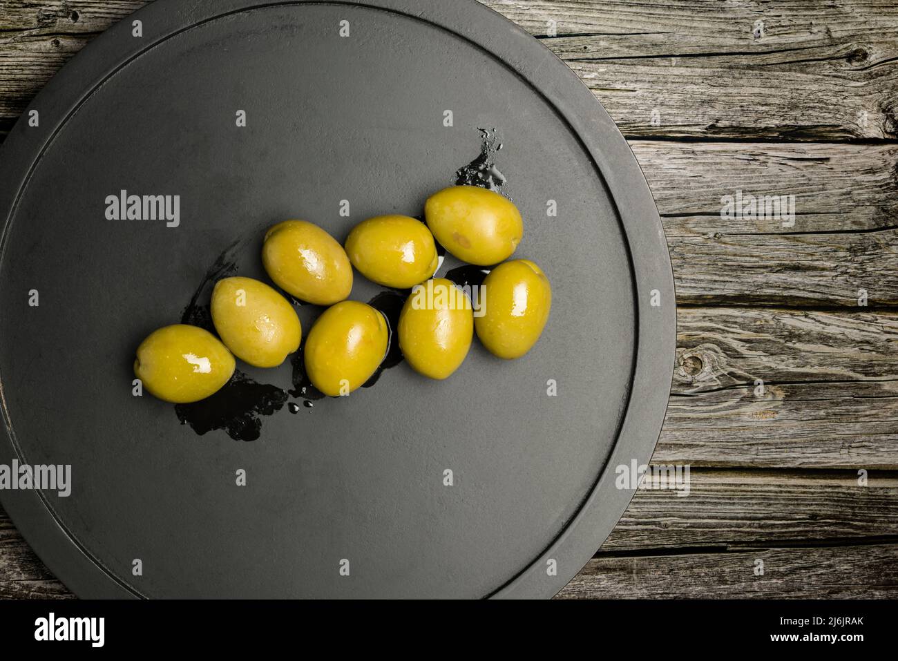 Big green olives on black plate on wooden table Stock Photo