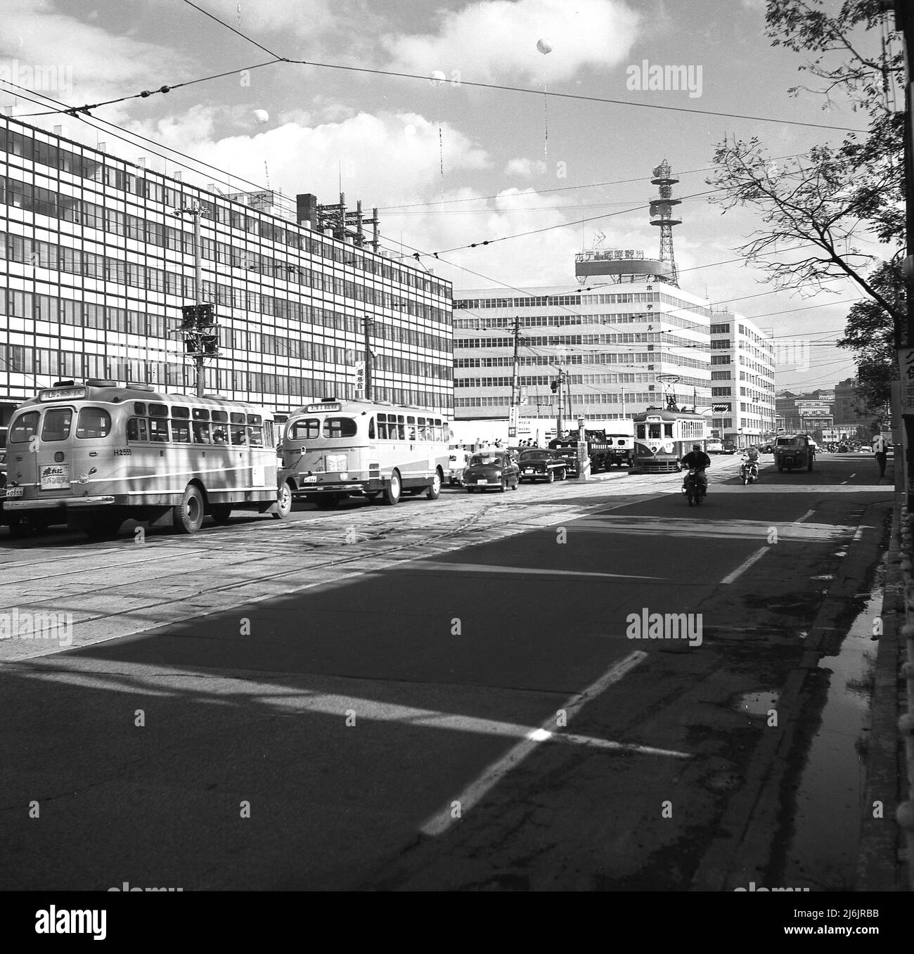 1960, historical, city street in Tokyo, Japan, showing coaches, cars and tram and modern office buildings. Stock Photo