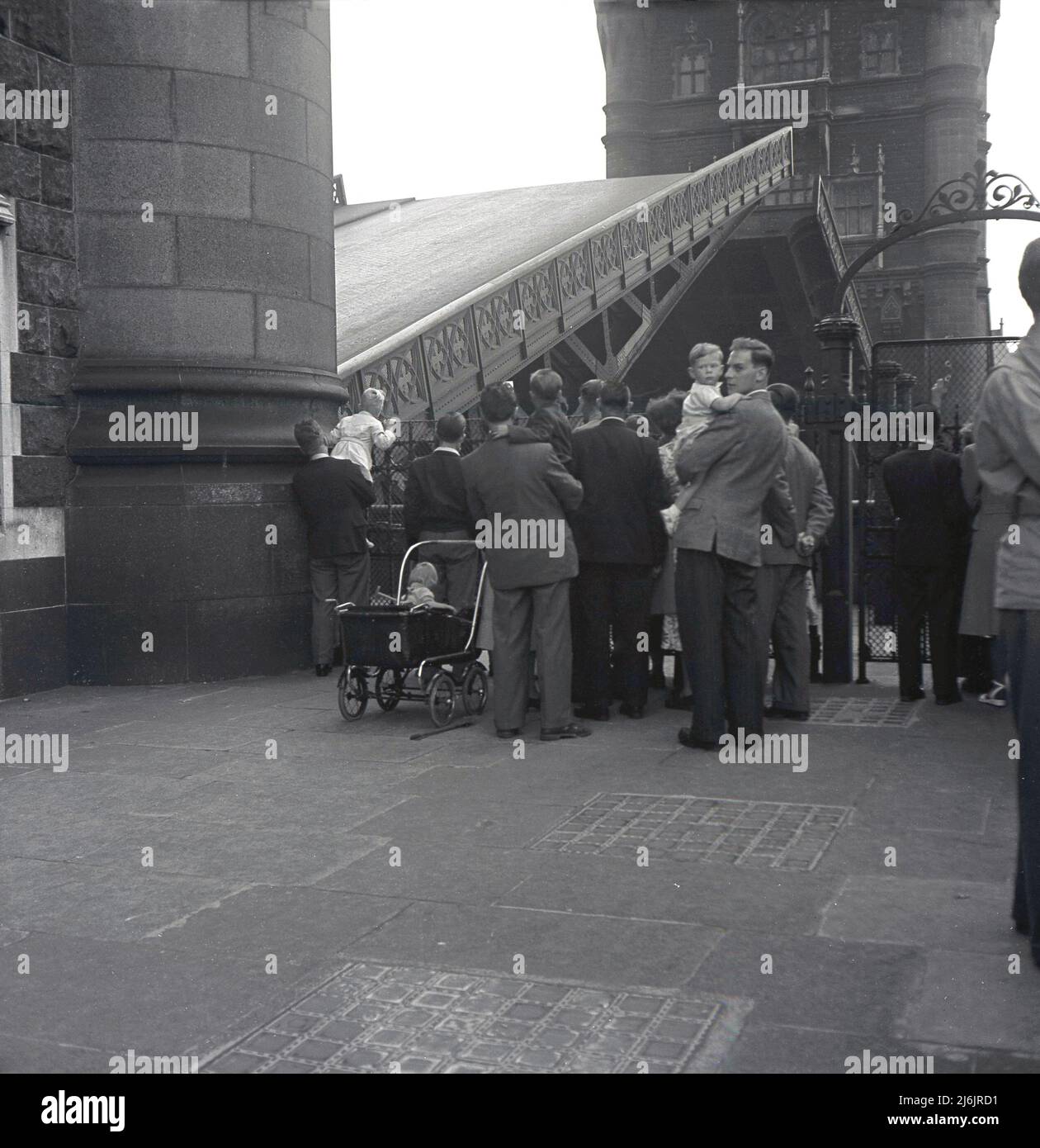 1953, historical, people gathered by one of the towers on Tower Bride watching the middle of the bridge being raised, London, England, UK. One of London's most famous atttractions, the combined bascule and suspension bridge crosses the River Thames and was opened in 1894. Stock Photo