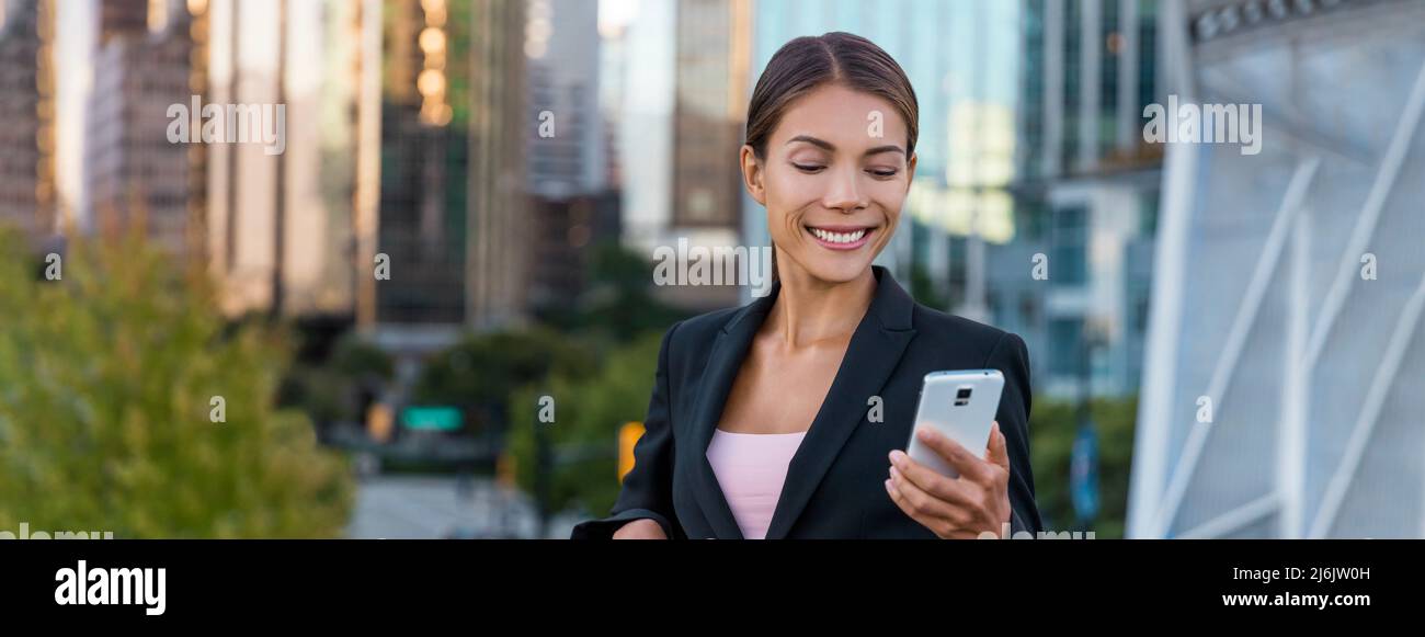 Woman sms texting using app on smart phone in city business district. Young business woman using smartphone smiling happy wearing suit jacket outdoors Stock Photo