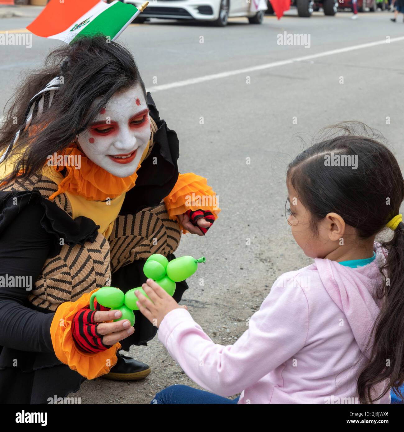 Detroit, Michigan USA - 1 May 2022 - A clown makes a balloon toy for a girl watching the Cinco de Mayo parade in Detroit's Mexican-American neighborhood. The annual parade returned in 2022 after a two-year hiatus due to the pandemic. Cinco de Mayo celebrates a Mexican victory over the French on May 5, 1862. Credit: Jim West/Alamy Live News Stock Photo