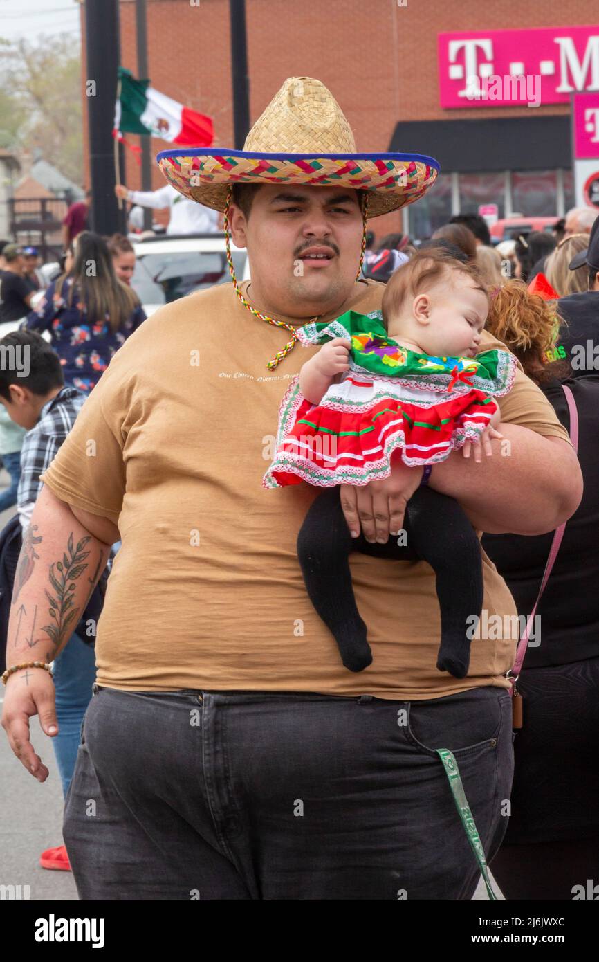 Detroit, Michigan USA - 1 May 2022 - A big man and a small baby watch (or sleep through) the Cinco de Mayo parade in Detroit's Mexican-American neighborhood. The annual parade returned in 2022 after a two-year hiatus due to the pandemic. Cinco de Mayo celebrates a Mexican victory over the French on May 5, 1862. Credit: Jim West/Alamy Live News Stock Photo