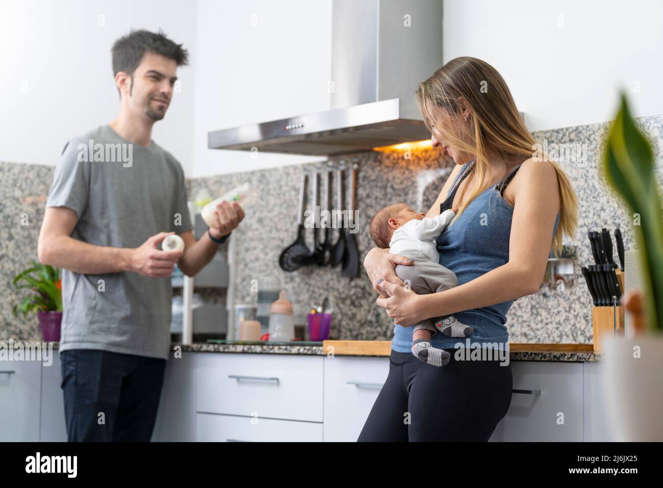 mother and father preparing a feeding bottle for their newborn in the kitchen Stock Photo
