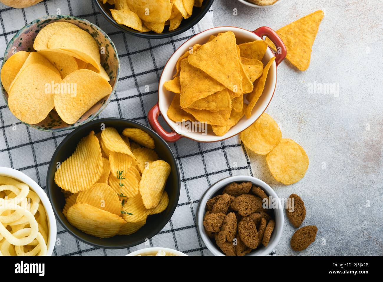 Snacks. Unhealthy food. All classic potato snacks with peanuts, popcorn and onion rings and salted pretzels in bowl plates on gray concrete background Stock Photo