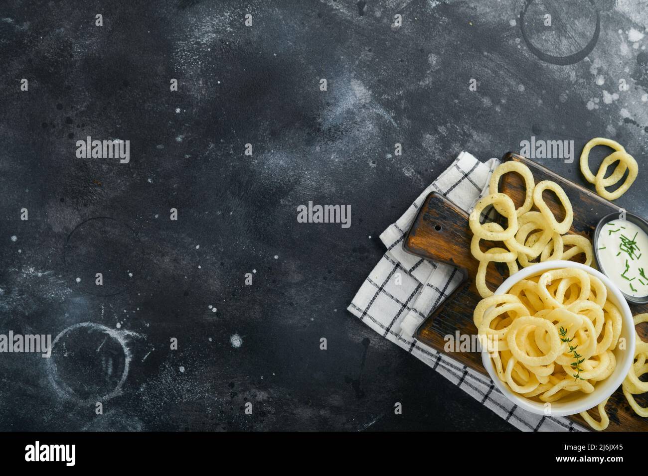 Onion rings. Fast food. Crispy onion chips in ceramic black bowl with sour cream sauce and onions in wooden stand on old black concrete background. Am Stock Photo