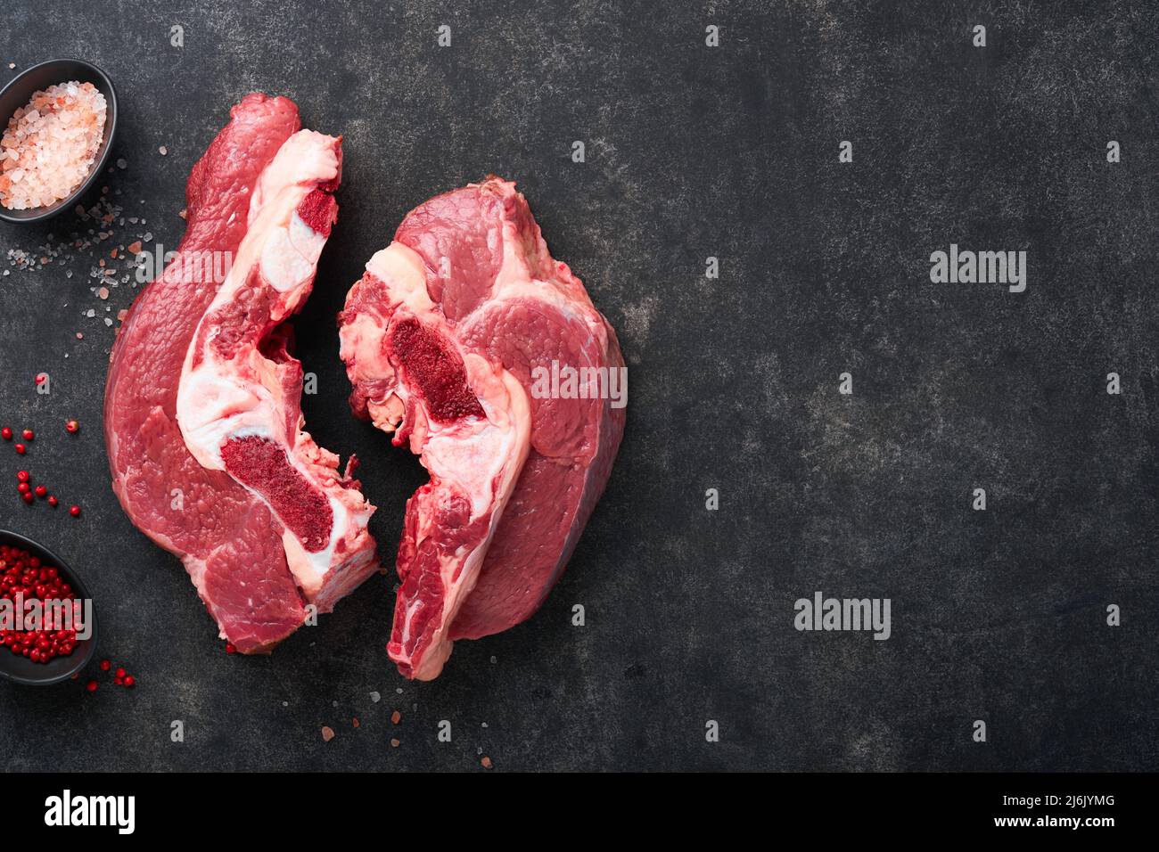 Raw beef meat. Rough piece of meat on bone for roast or soup with salt, pepper, thyme and rosemary on a black concrete background. Entrecote. Raw cowb Stock Photo