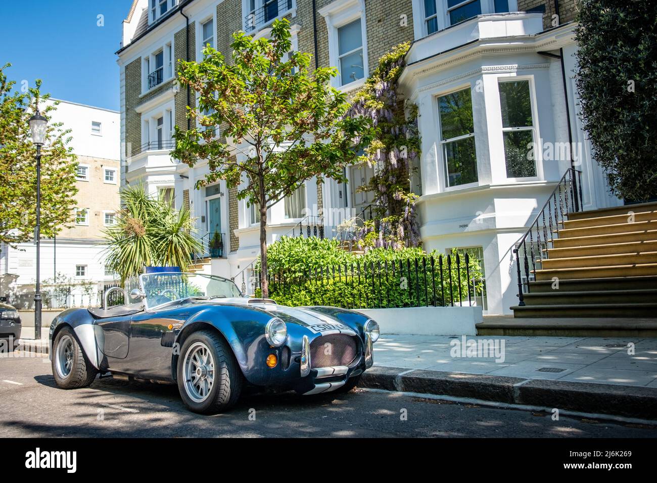 London- An AC Cobra sports car parked outside attractive street of terraced houses Stock Photo