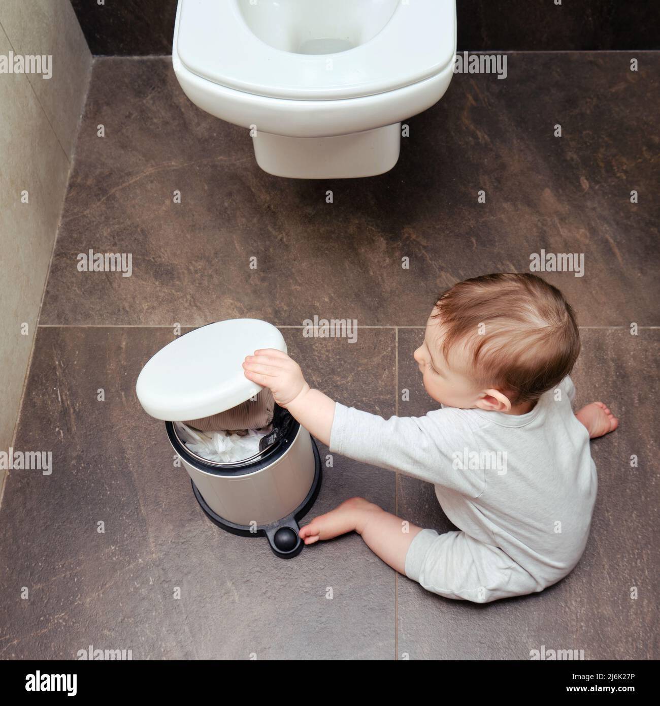 Toddler baby boy is playing in the toilet room with a trash can. Child ...