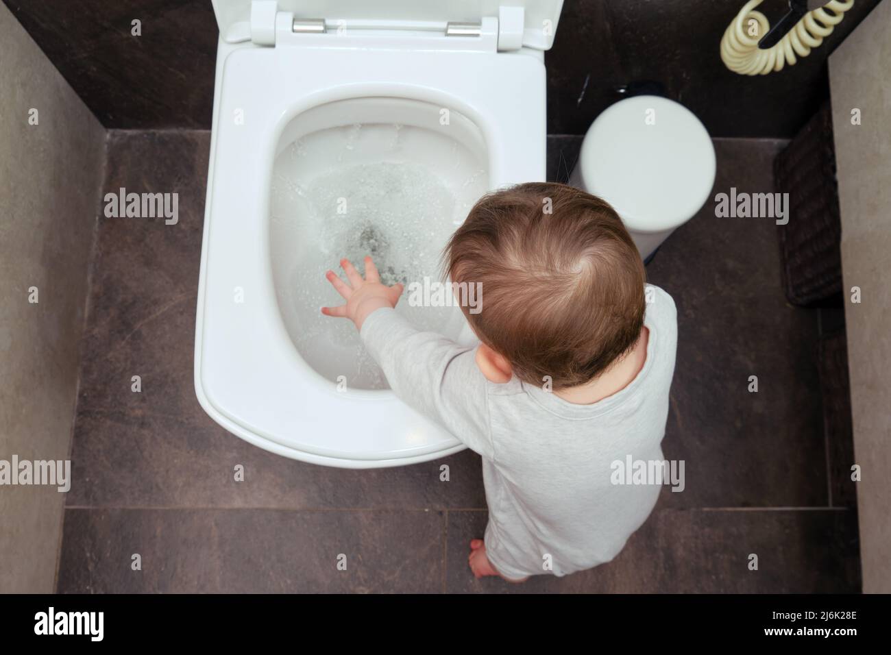 Toddler baby boy is playing in the toilet room with water flush in the