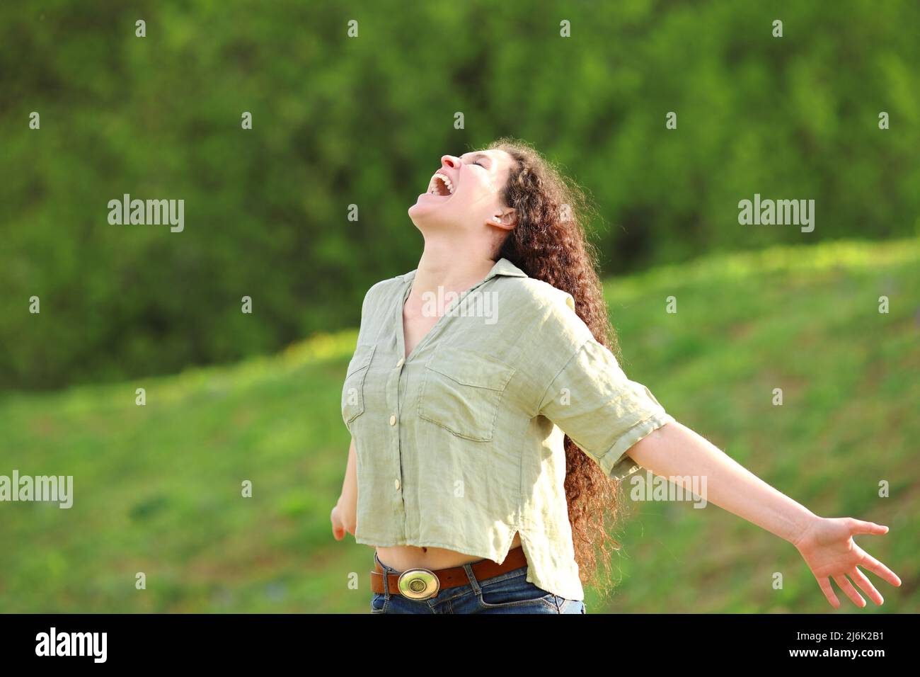 Happy woman screaming to the air in a green park outstretching arms ...