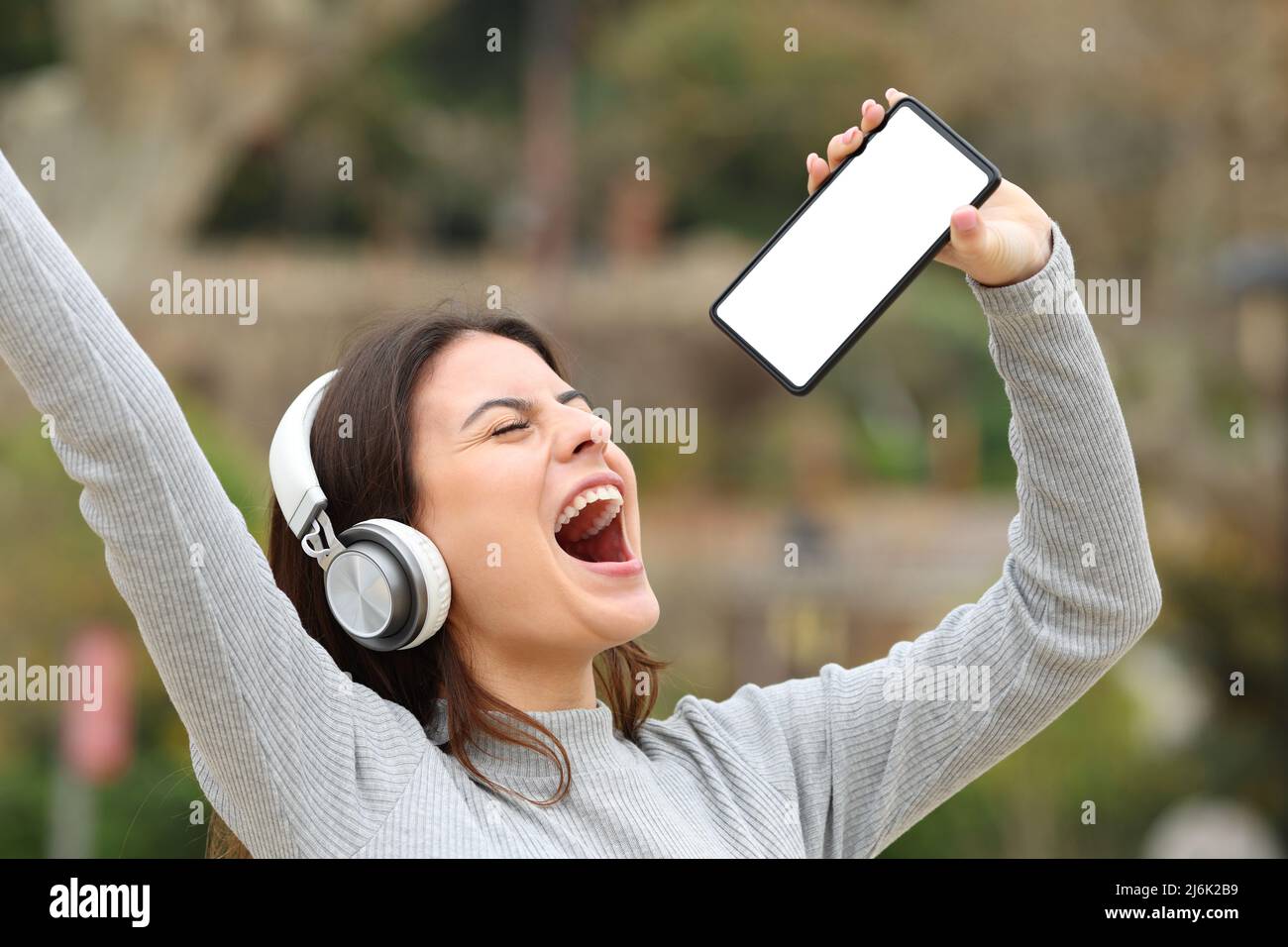 Happy teen singing showing smart phone blank screen in a park Stock Photo