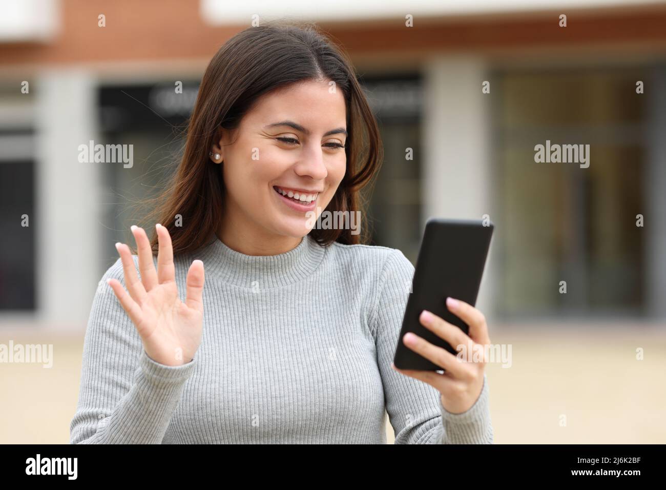 Happy teen greeting during a videocall walking in the street Stock Photo