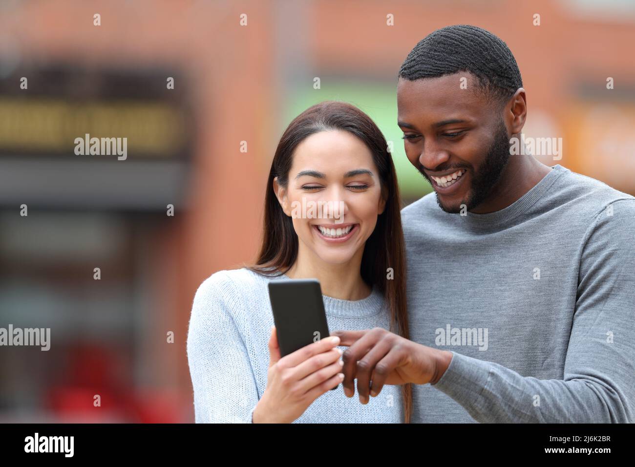 Front view portrait of a happy interracial couple consulting phone text in the street Stock Photo