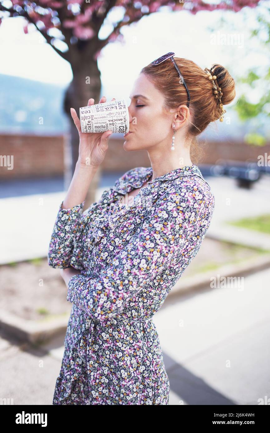 Young redhead woman drinking coffee outdoors from plastic cup Stock Photo