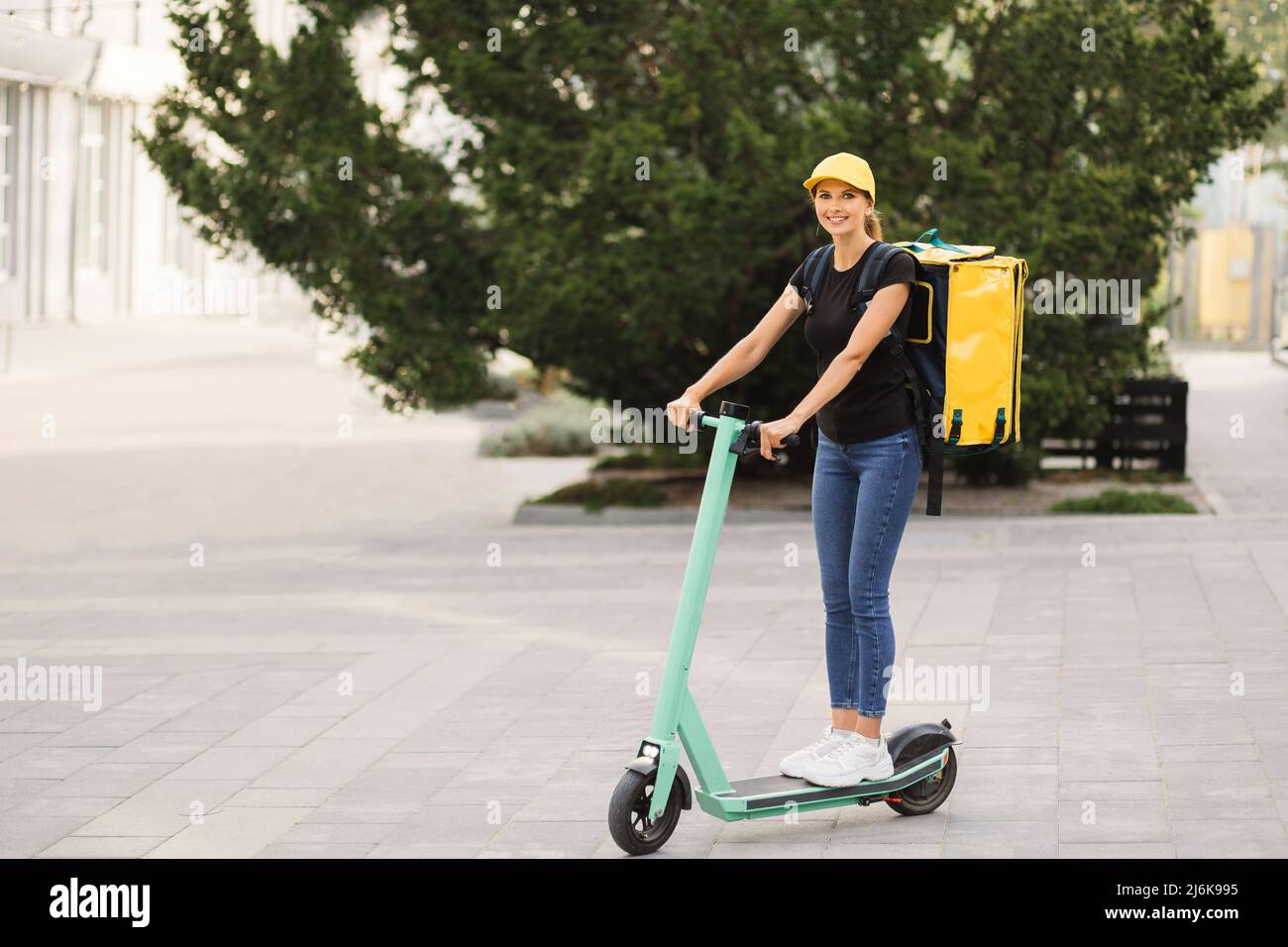 Beautiful young girl with a yellow bag on her back and cap riding an  electric scooter