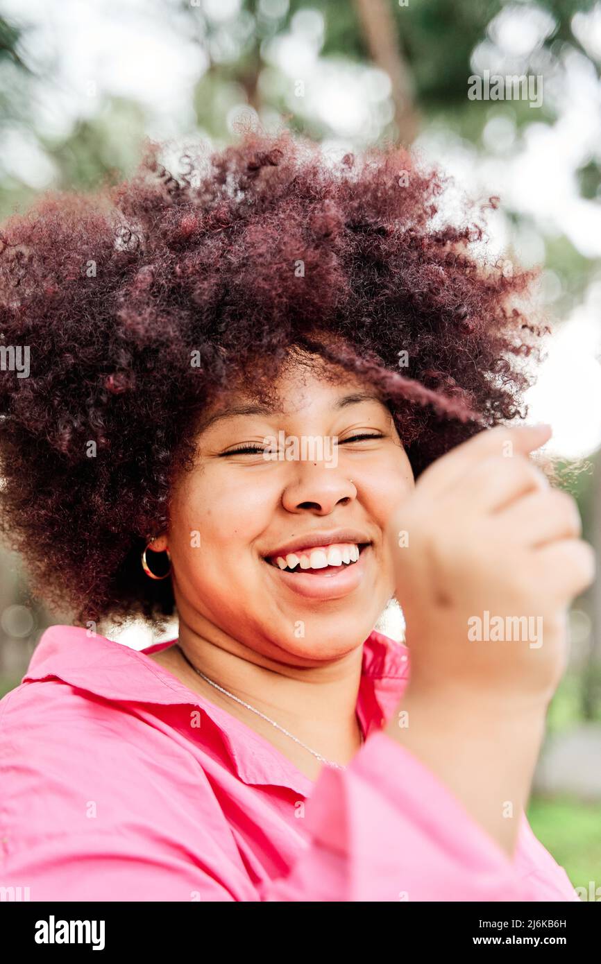 young, modern girl holds a lock of curly hair in her hand. african