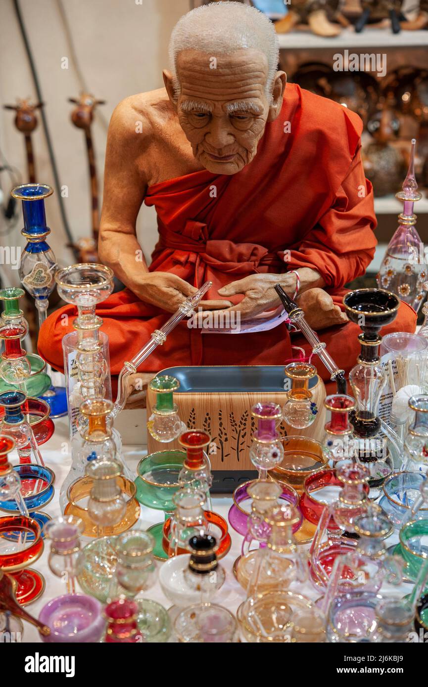 Buddhist monk life-size puppet, in orange robes sitting in meditation on a market stall. Water pipes hookah in the foreground. Stock Photo