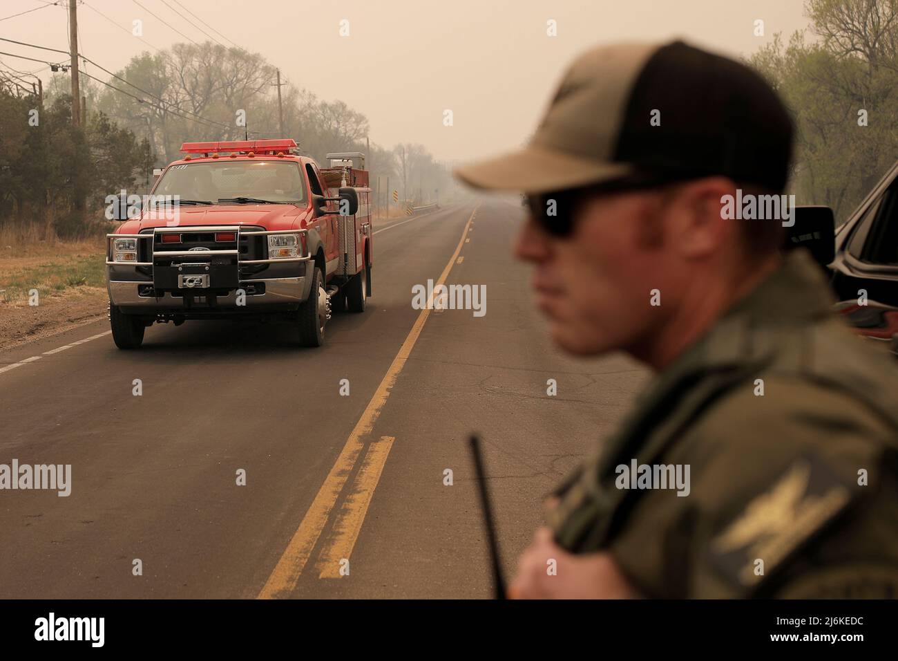 A fire truck approaches a police road block as smoke spreads from the