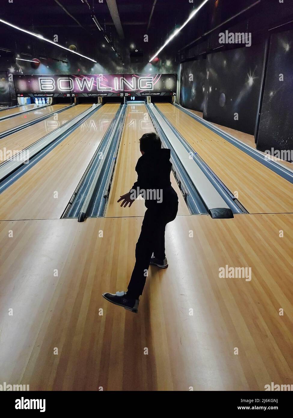 A teenage boy plays bowling, throws the ball into the skittles. Back