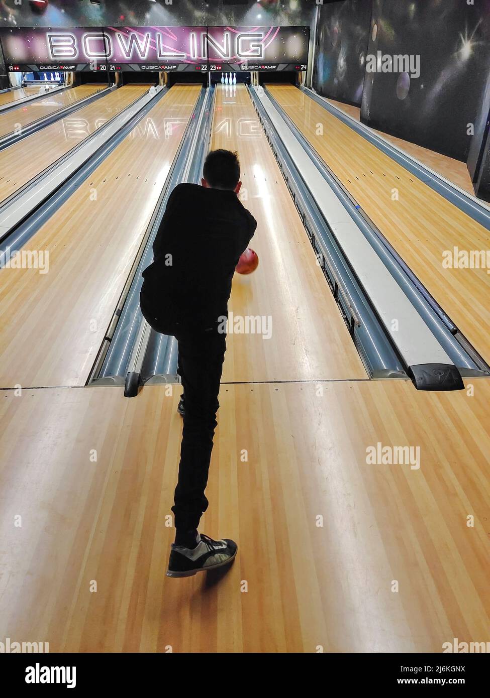 Guy teenager plays bowling, swings and throws the ball into the skittles. Back view in perspective Stock Photo