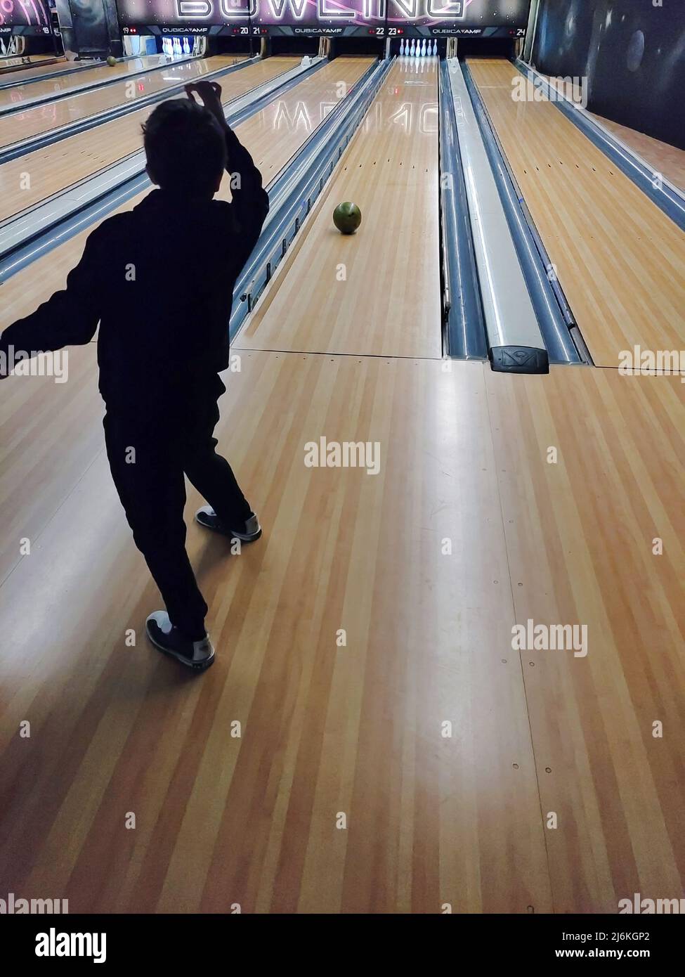 A teenage boy plays bowling, throws the ball into the skittles. Back