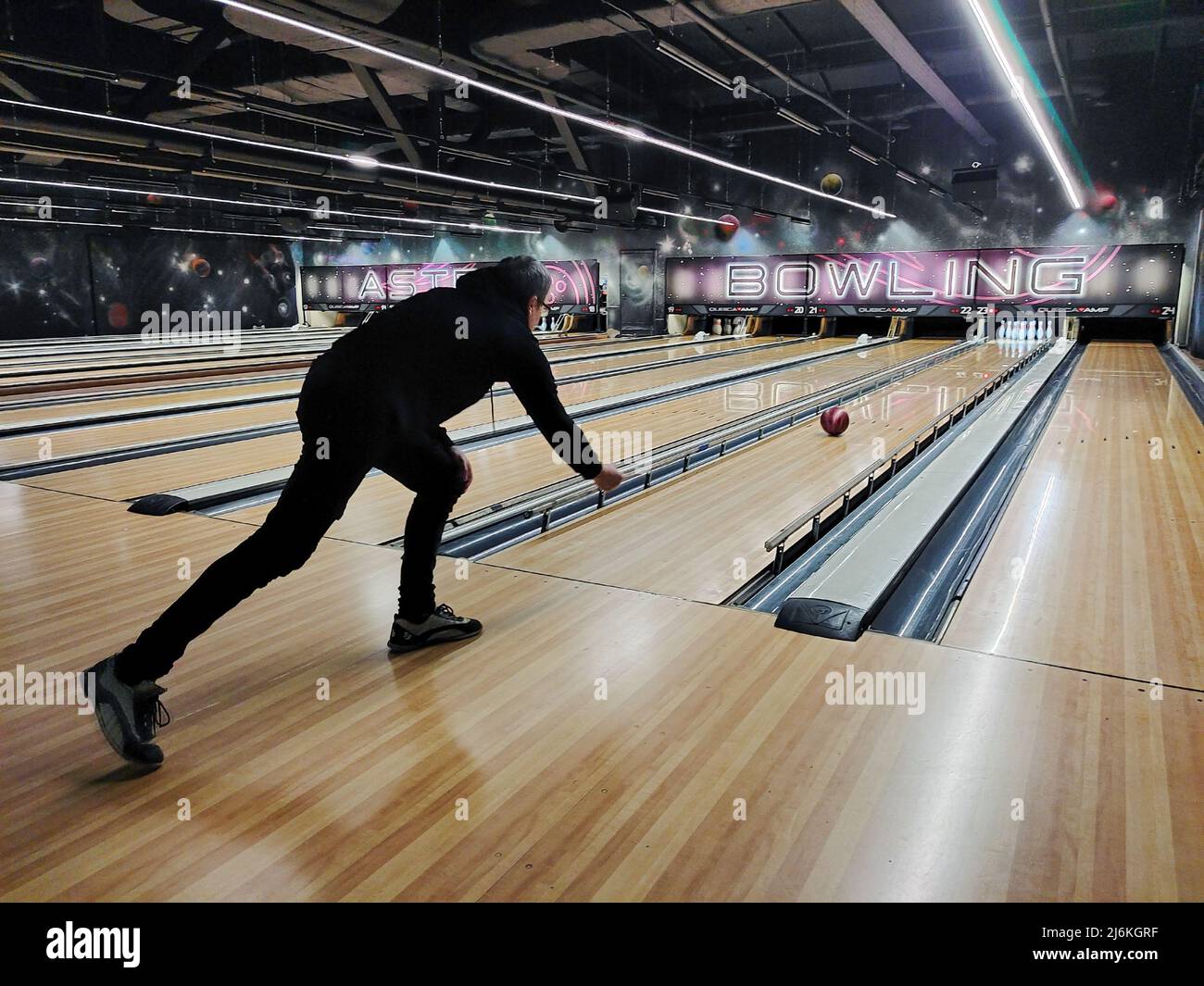 A man plays bowling, swings and throws the ball into the skittles. Back