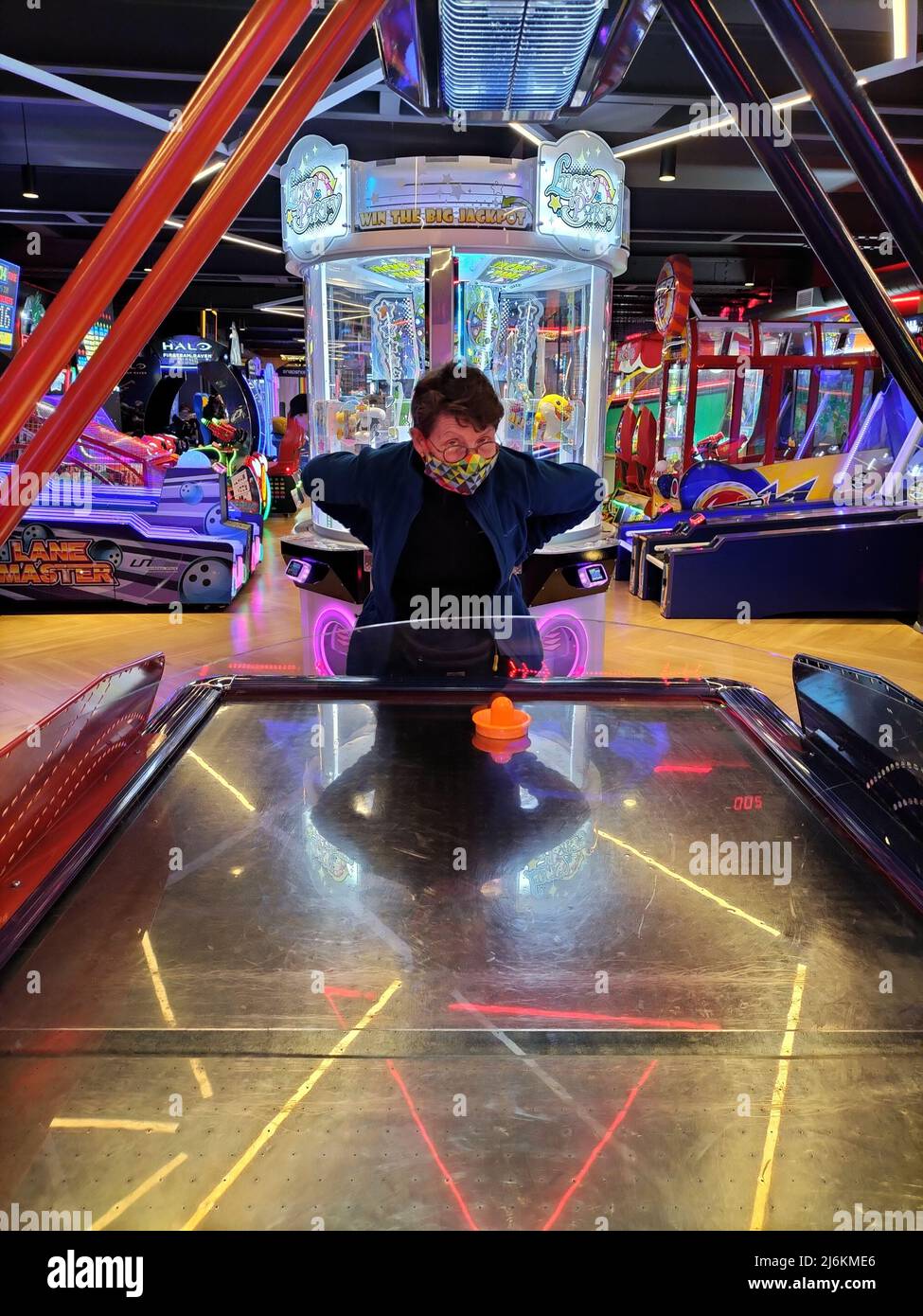 Middle aged masked woman playing air hockey in a Timezone games arcade Stock Photo