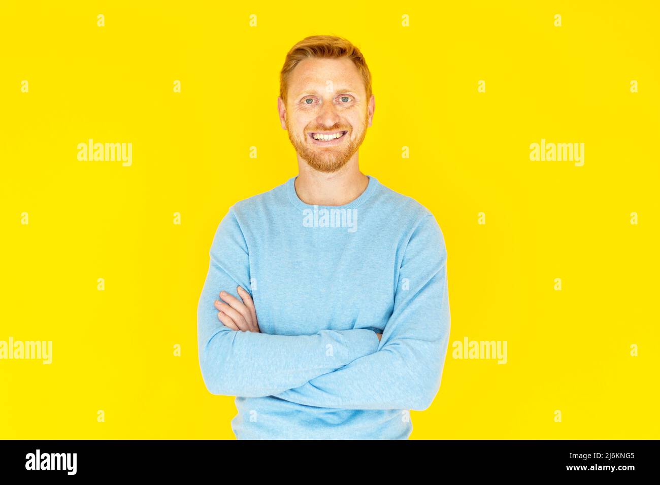 Redhead young man with crossed arms standing isolated over yellow background Stock Photo