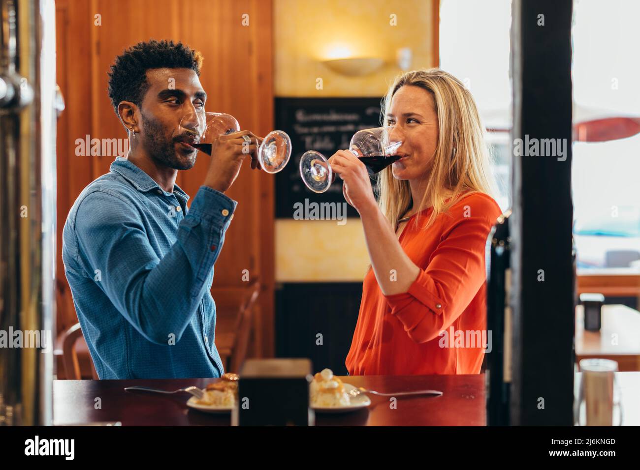 multiethnic couple look at each other with feeling while drinking red wine from their glasses
