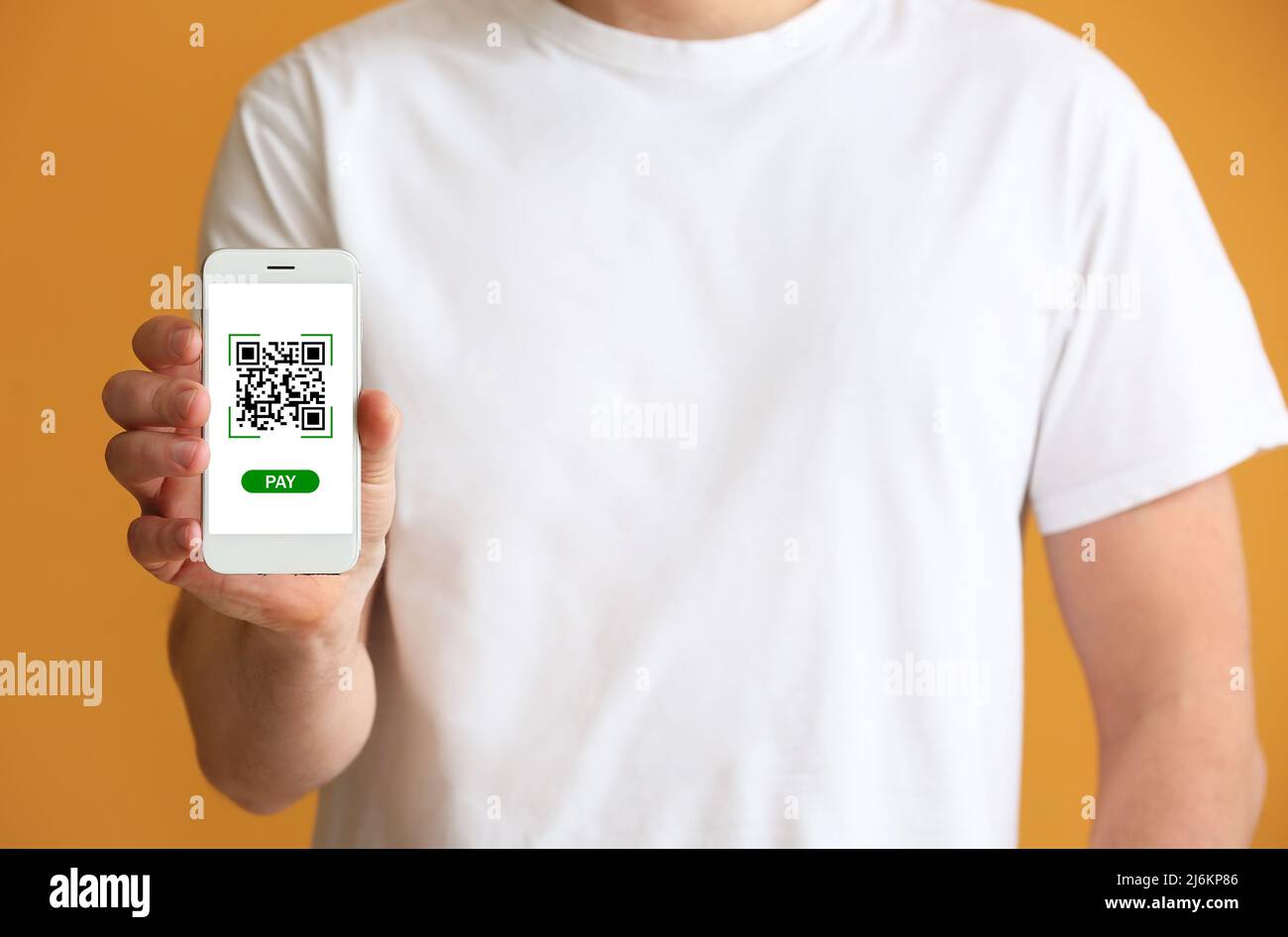 Man holding smartphone with QR code on screen against orange background, closeup Stock Photo