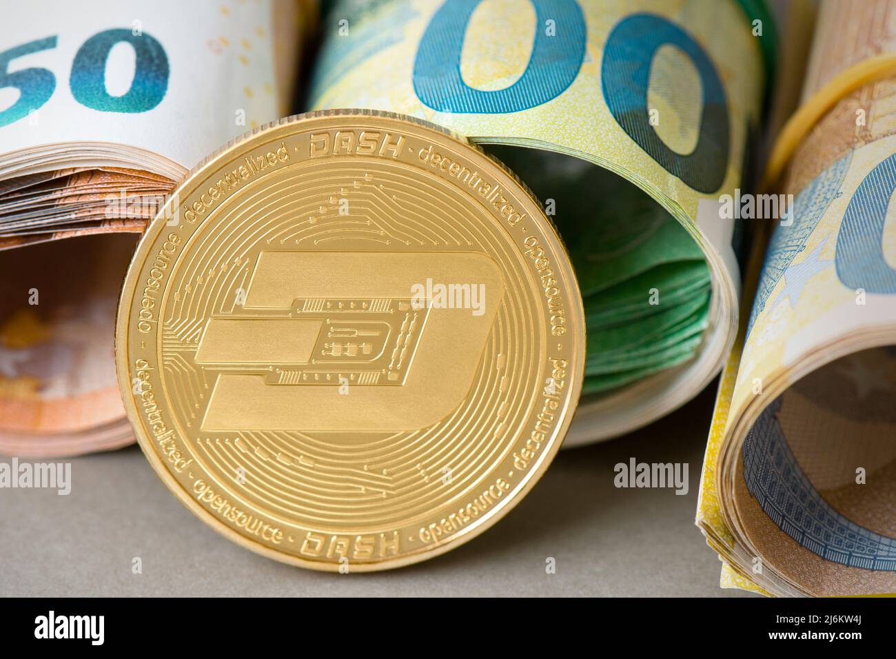 Cryptocurrency Dash golden coin on the background of rolled euro bills. Currency exchange for e-commerce, saving money, transfers concept. Financial Stock Photo