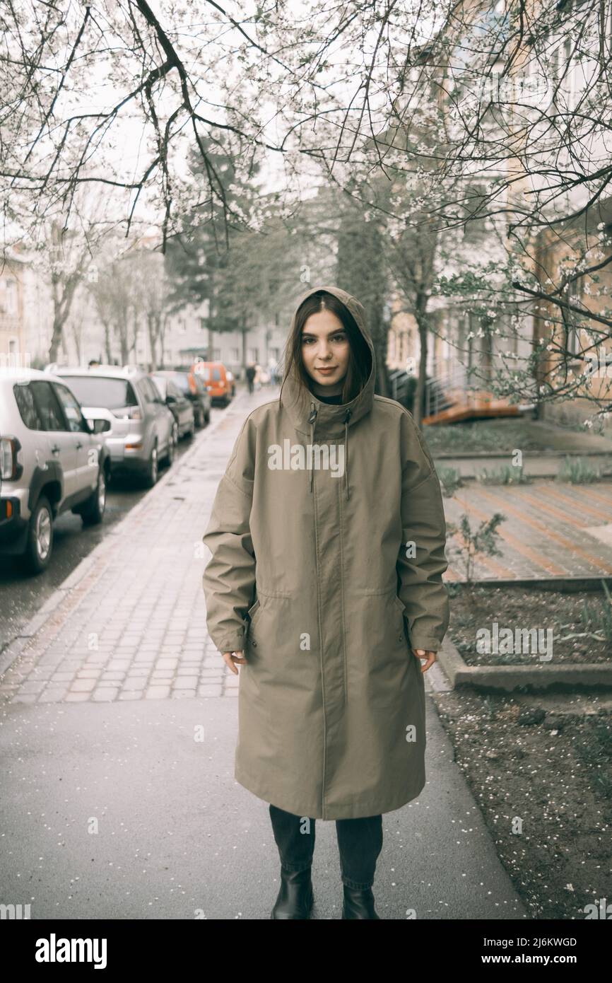 Traveling young woman in green raincoat with hood walking down street ...