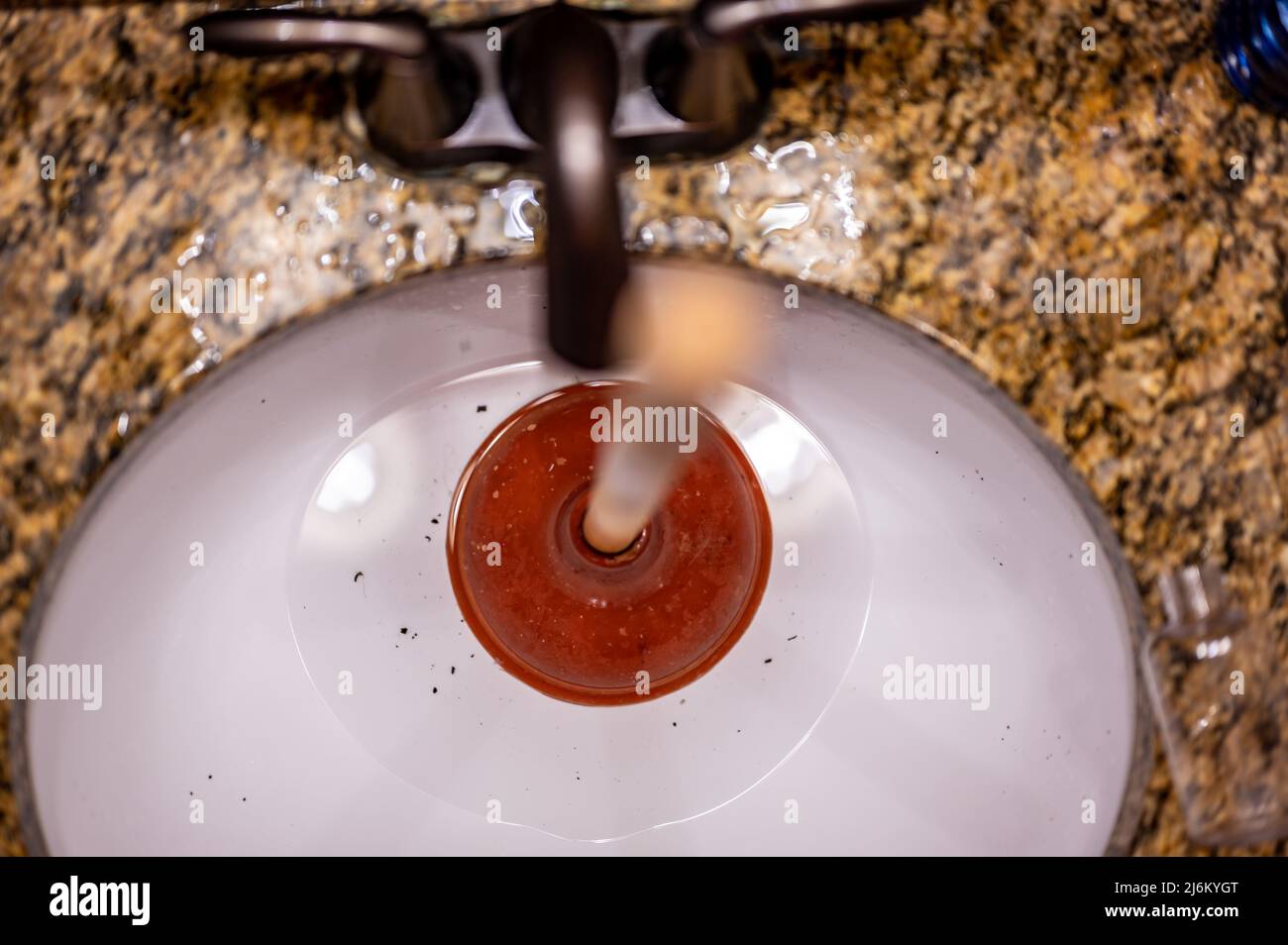 Using a plunger on a bathroom sink plugged with Hair and scum in a pool