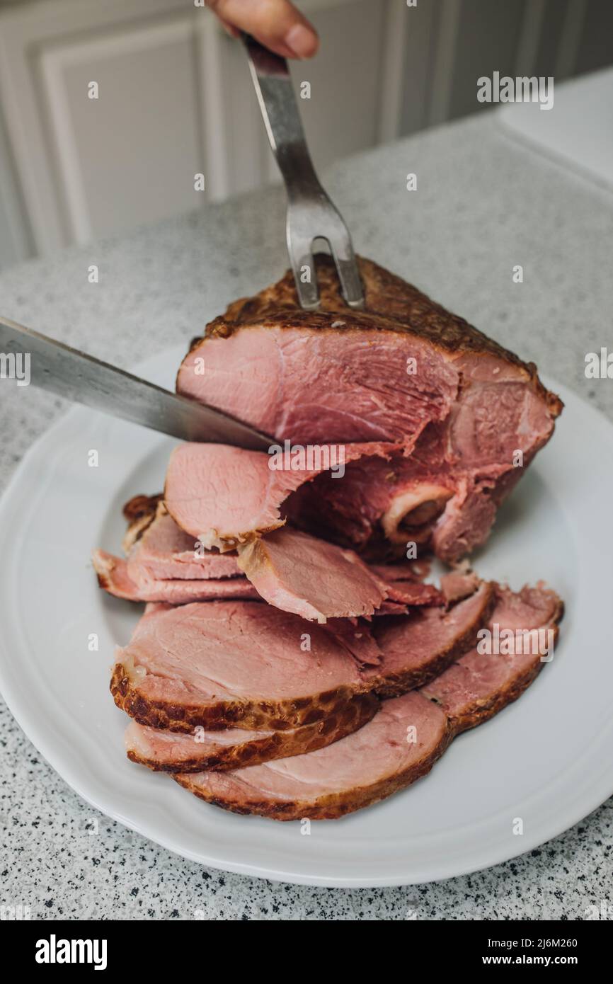 hand slicing Kurobuta bone-in ham meat on kitchen counter with knife and fork Stock Photo