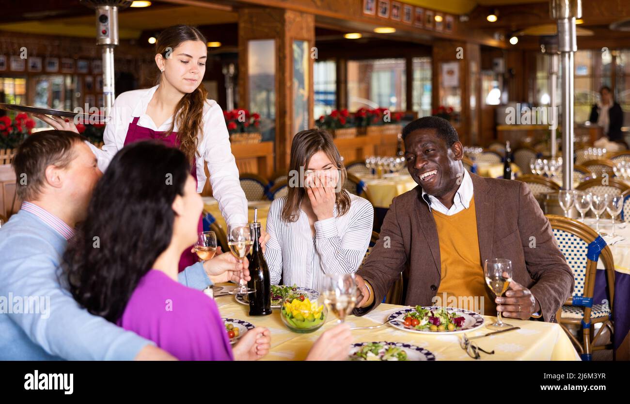Young waitress serving cheerful people during dinner in restaurant Stock Photo