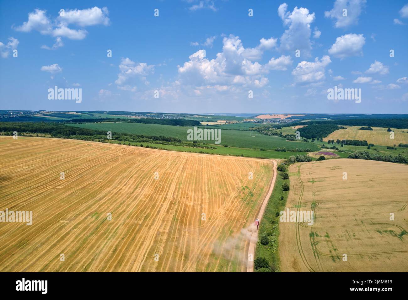 Aerial view of cargo truck driving on dirt road between agricultural wheat fields making lot of dust. Transportation of grain after being harvested by Stock Photo