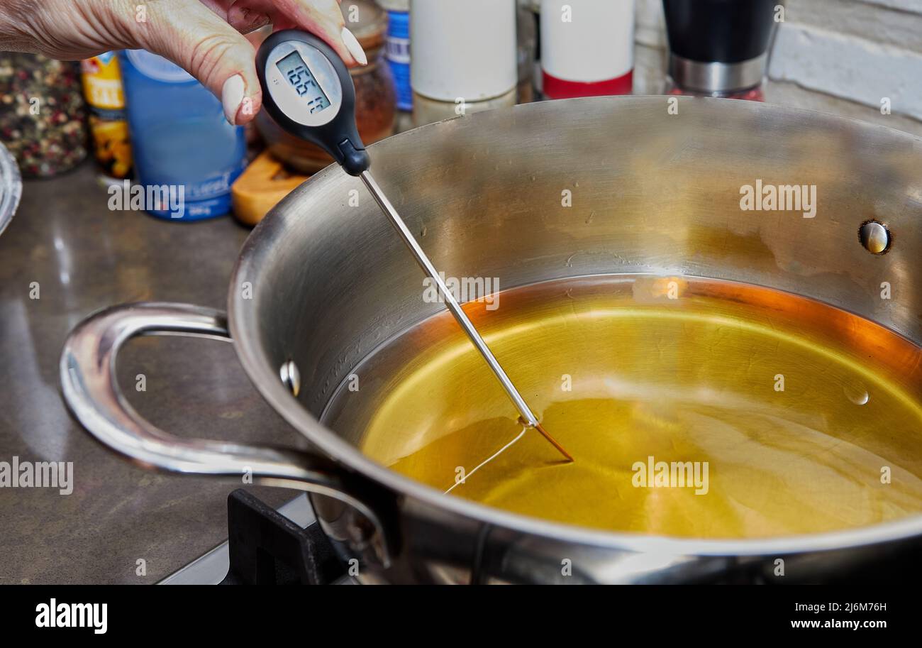 Chef checks the temperature of the heated oil in pot on gas stove with