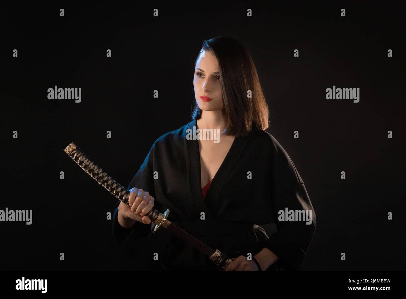 Portrait of young kung fu brunette woman with katana on black background. Stock Photo