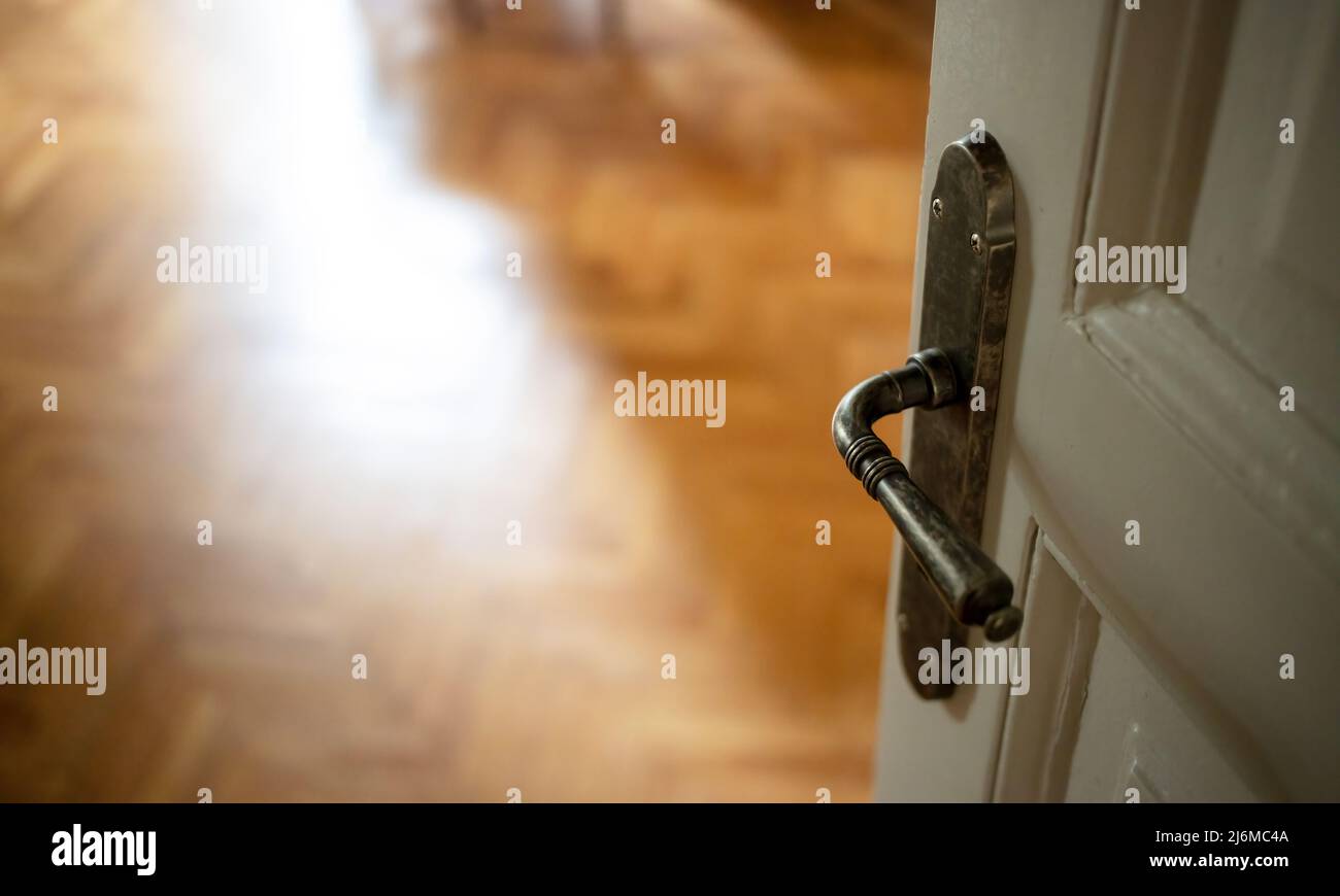 Door open close up view. Retro doorknob on white vintage wooden door, blur empty wood floor parquet, classy house room interior Stock Photo