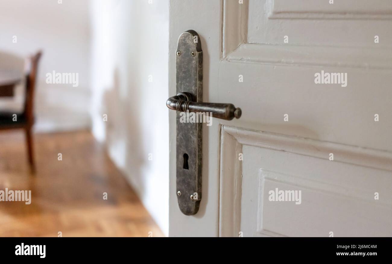 Door open close up view. Retro doorknob on white vintage wooden door, blur floor parquet, classy office interior Stock Photo