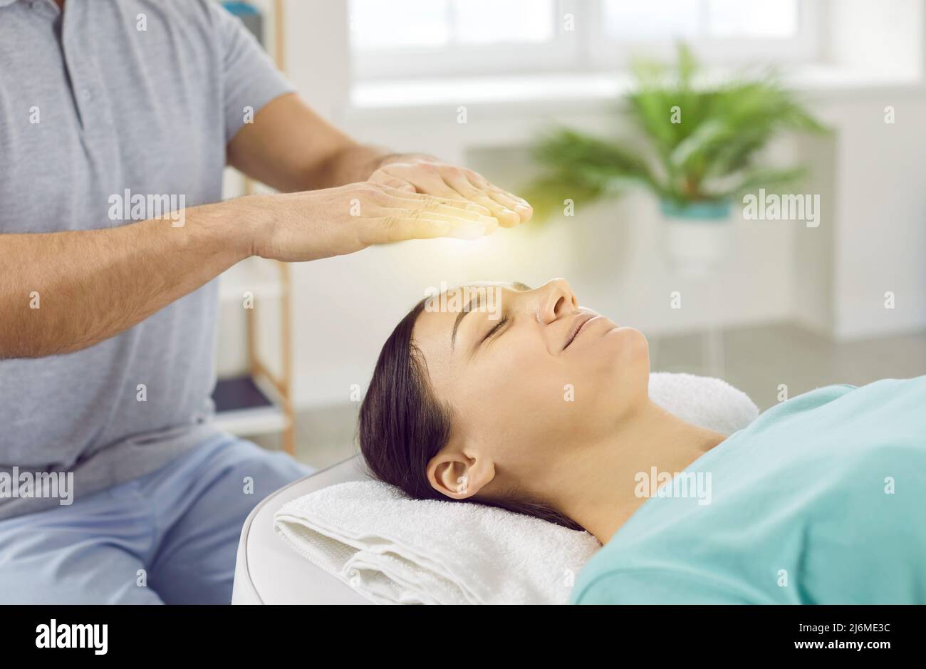 Happy relaxed and calm young woman with closed eyes receiving reiki treatment above head. Stock Photo
