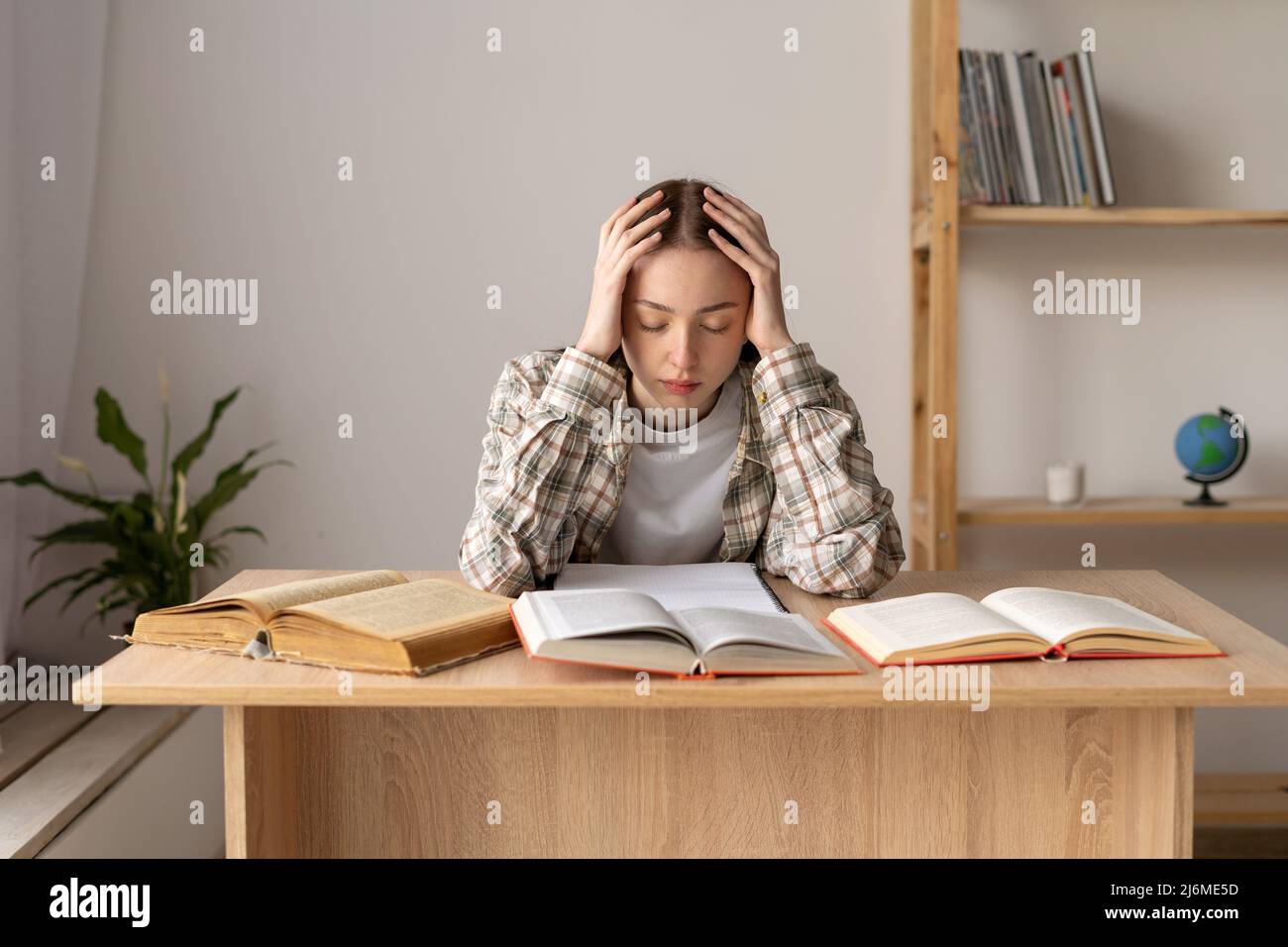 Tired exhausted caucasian female student sitting in a library with books closed her eyes massaging her head, headache and stress from study Stock Photo