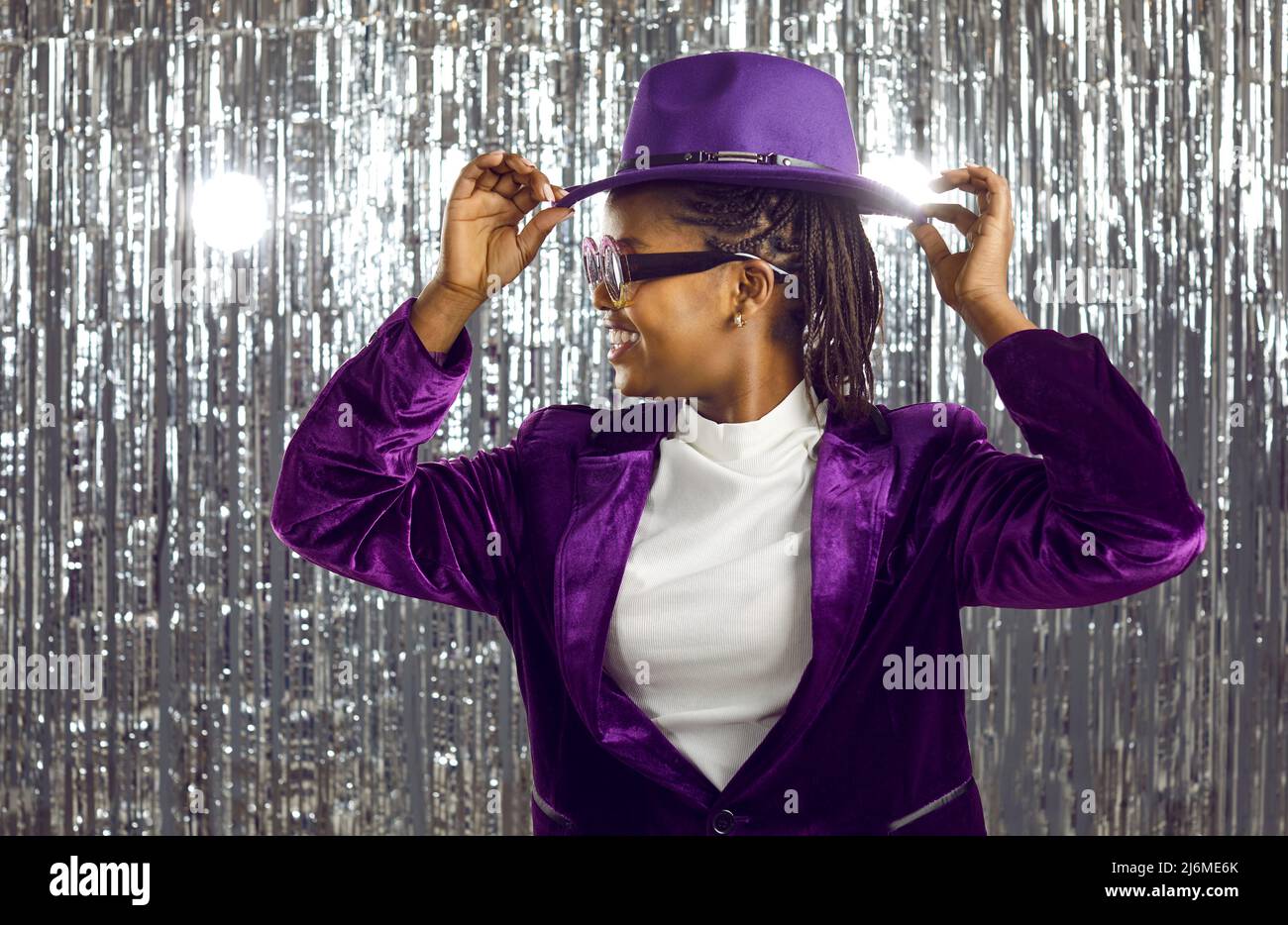 Happy cheerful young black woman in purple hat dancing and having fun at disco party Stock Photo