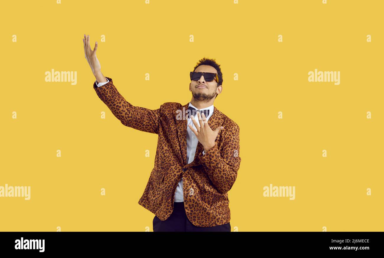 Funny black man in a leopard suit and cool sunglasses dancing isolated on a colour background Stock Photo